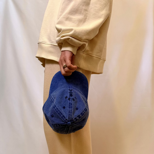 IRBN stone wash cap in Marina Blue being held at side, shown with Cannoli Cream sweatshirt, one size