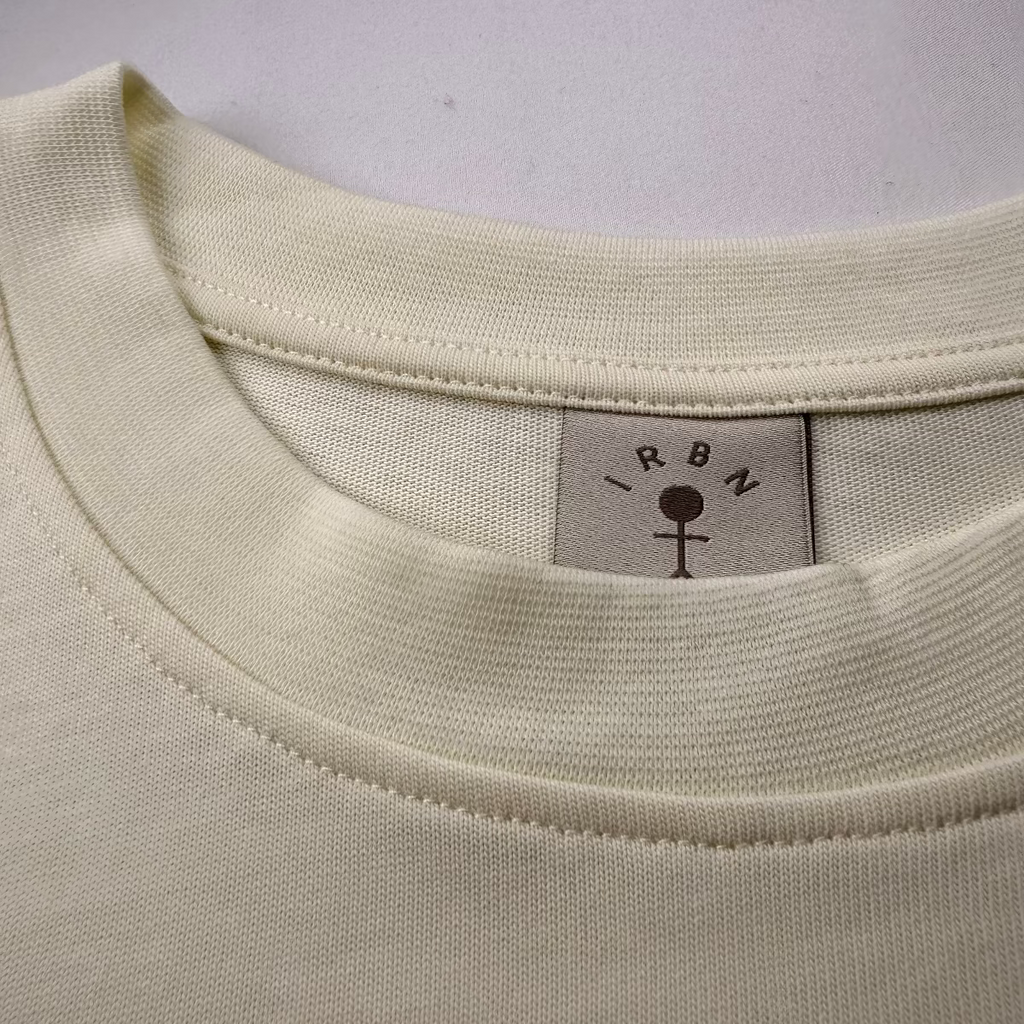 Close-up of woven IRBN neck label on Cannoli Cream boxy t-shirt, GOTS-certified organic cotton made in Portugal