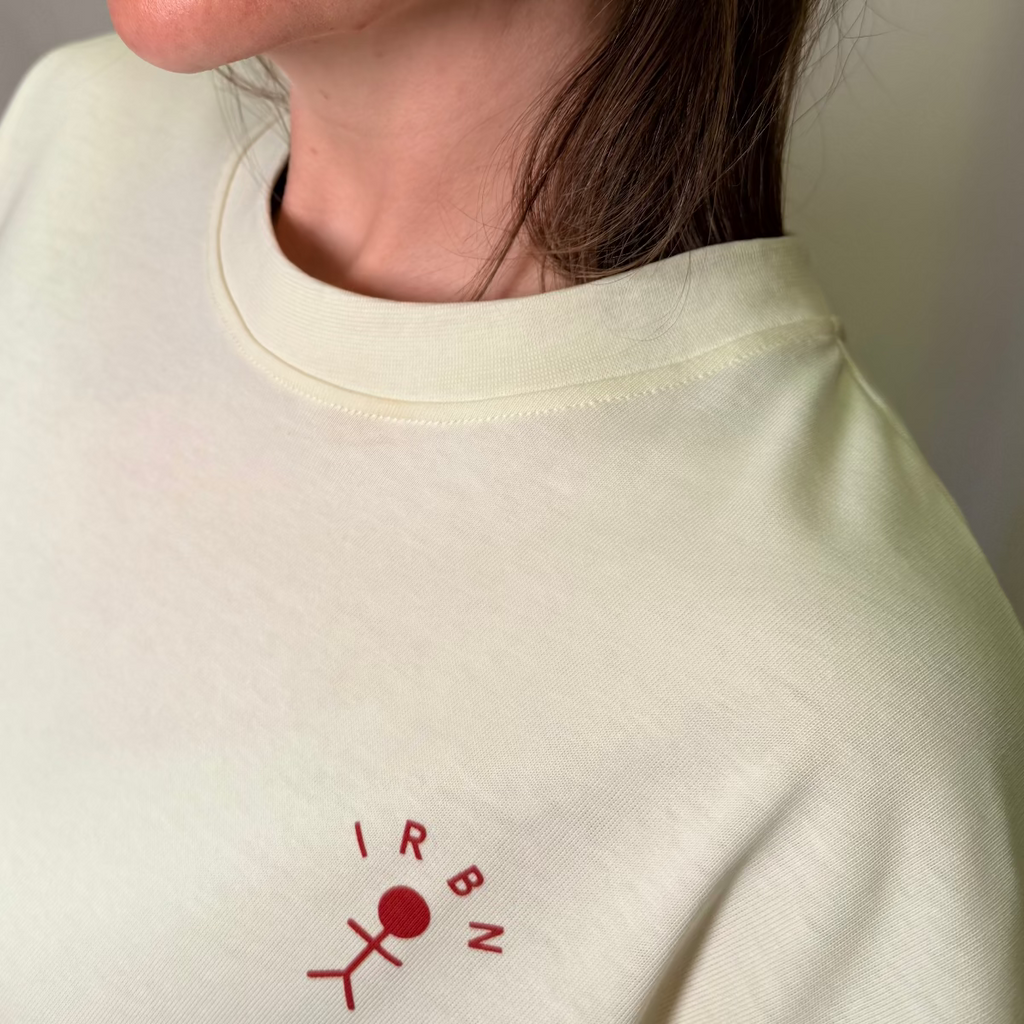 Close-up of embroidered IRBN stick figure logo on chest of Cannoli Cream boxy t-shirt, 250gsm GOTS-certified organic cotton